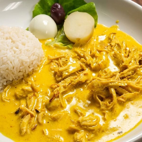 Aji de Gallina, a Peruvian dish with shredded chicken in yellow sauce, rice, potatoes, egg, and olive.