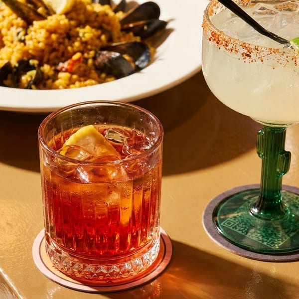 Paella with mussels, a red cocktail, and a margarita in a cactus glass on a table.