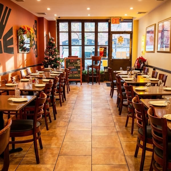 Empty restaurant dining room with set tables, orange and cream walls, and a Christmas tree near the entrance.