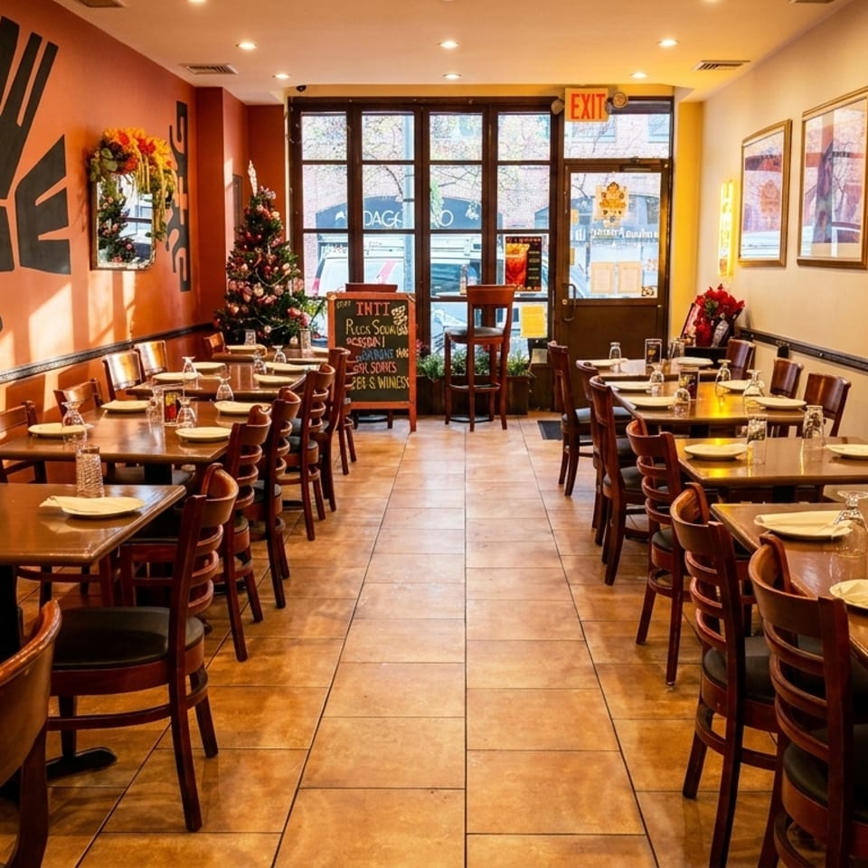Empty restaurant dining room with set tables, orange and cream walls, and a Christmas tree near the entrance.